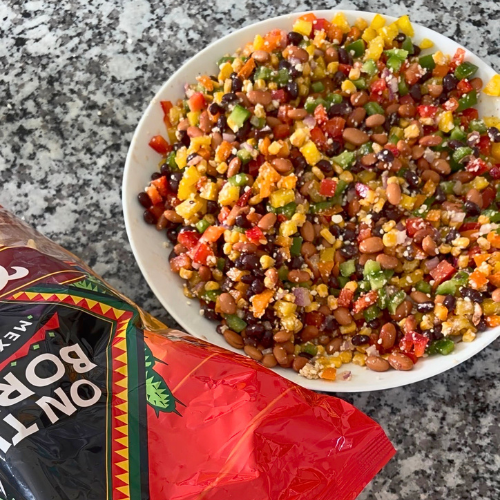 White bowl filled with cowboy caviar salad with a bag of tortilla chips next to it