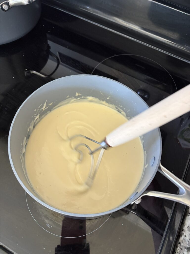 Creamy cheese sauce being whisked in a saucepan on the stove