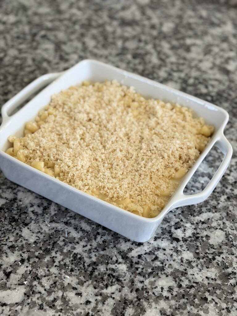 Unbaked mac and cheese topped with Parmesan bread crumbs in a white baking dish