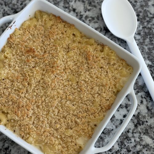 Baked mac and cheese with a golden Parmesan crumb topping in a white baking dish with a serving spoon
