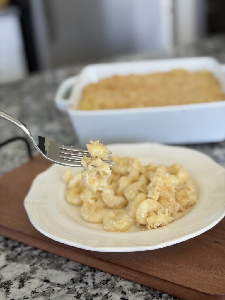 Forkful of creamy baked mac and cheese over a plate, with the baking dish in the background